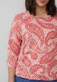 Gemusterter Oberteil mit einem rosa und cremefarbenen Design und abstrakten Formen. Rundhalsausschnitt und Dreiviertelärmel, aus weichem Stoff gefertigt.