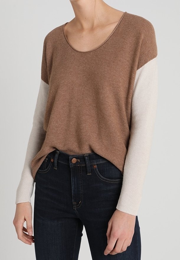 Brauner Pullover mit cremefarbenen Ärmeln, runder Ausschnitt, weiche Textur, entspannte Passform, kombiniert mit dunklen Jeans, die einen lässigen Look präsentieren.