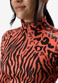 Top sportivo con zip di colore arancione con strisce zebrate nere, dotato di collo alto e vestibilità moderna. Il materiale appare liscio e elegante.