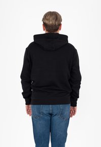 Felpa nera con cappuccio e tasca a marsupio, con polsini e orlo a costine. Indossata con jeans di denim blu, vista da dietro su uno sfondo bianco.