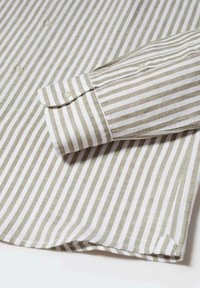 Košile s límečkem a zapínáním na knoflíky s horizontálními pruhy v olivově zelené a bílé barvě. Bavlněná tkanina s hladkou texturou a detaily s ohrnutým manžetem.