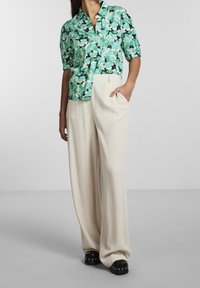 Chemise à manches courtes florale en vert et noir, associée à un pantalon large crème ; chaussures à plateforme noires avec des clous en argent. Textures lisses.