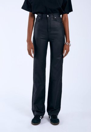 Pantalon noir taille haute à jambes droites porté avec des baskets noires et un haut noir, accessoirisé avec un bracelet et une bague en argent.