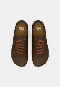 Ruskeat nahkakengät, joissa on ruskeat nauhat, pyöreät kärjet ja minimalistinen muotoilu. Sisäpuolella näkyy "PEU CAMI CAMPER" ja "Made in Europe" -etiketit.