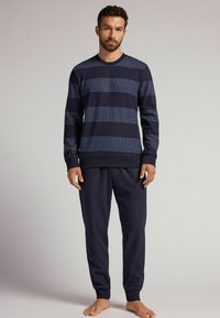 Marineblaues Langarmshirt mit gestreiftem Muster in horizontalen hellen und dunklen Blautönen, kombiniert mit passenden marineblauen Hosen. Weicher, strukturierten Stoff.