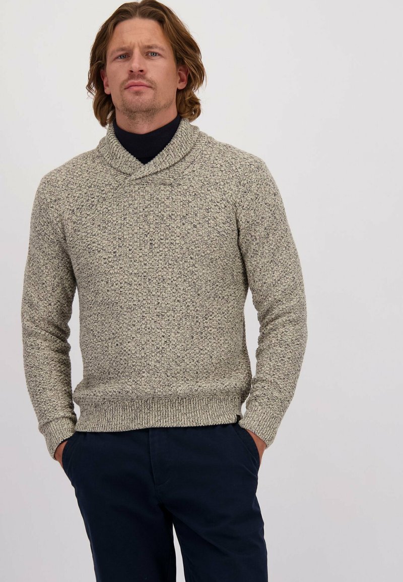 Pull en tricot gris clair avec des taches foncées, doté d'un col châle et de poignets et d'un ourlet côtelés. Assorti avec un pantalon bleu marine.