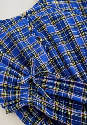 Blue plaid fabric with pink, yellow, and green lines. Features gathered sleeves and a wooden button detail at the neckline.