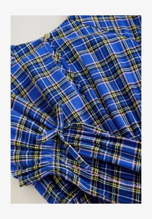 Tissu à carreaux bleu avec des lignes roses, jaunes et vertes. Présente des manches froncées et un détail de bouton en bois au niveau de l'encolure.