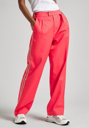 Pantaloni larghi corallo brillanti con vita alta, pieghe e strisce laterali dorate, realizzati in tessuto morbido, abbinati a sneaker bianche.