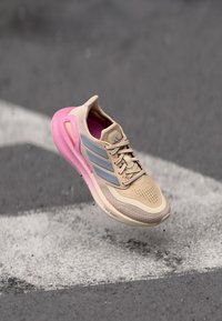 Beige running shoe featuring a breathable upper, pink midsole, grey accents, and perforated texture for ventilation.