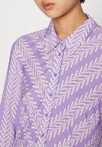 Lavendel skjorta med knapp up, pryd med ett vitt zigzag-mönster, med klassisk krage och små knappar. Mjuk tygtextur, figursydd design.