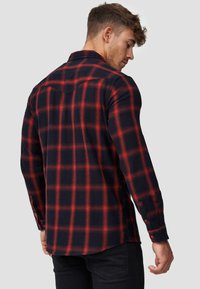 Camisa de franela a cuadros rojos y negros con mangas largas, puños abotonados y cuello puntiagudo. Presenta un corte holgado y una textura suave.