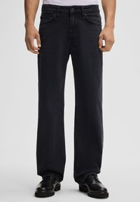 Schwarze Denim-Hosen mit lockerer Passform, featuring ein traditionelles Fünf-Taschen-Design und gestickte Akzente. Glatte Textur und robuster Stoff.