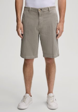 Pantaloni corti beige con un motivo testurizzato, dotati di una vita con bottone, tasche frontali e orli arrotolati, abbinati a sneakers bianche.