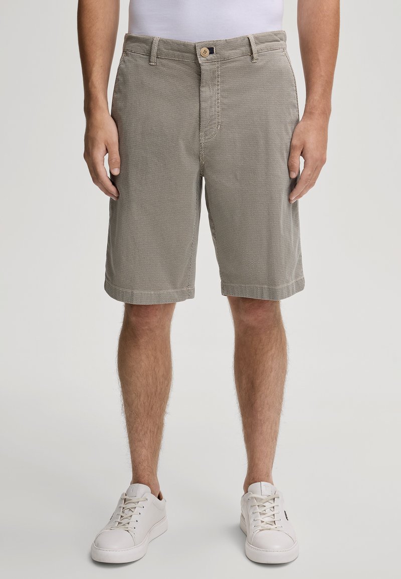 Pantaloni corti beige con un motivo testurizzato, dotati di una vita con bottone, tasche frontali e orli arrotolati, abbinati a sneakers bianche.