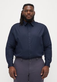 Camicia a maniche lunghe blu navy con collo e bottone frontale. Realizzata in tessuto liscio, presenta una vestibilità su misura e polsini con bottone.