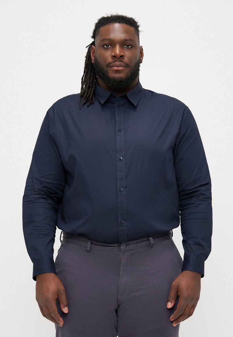 Camicia a maniche lunghe blu navy con collo e bottone frontale. Realizzata in tessuto liscio, presenta una vestibilità su misura e polsini con bottone.