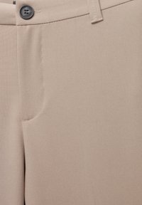 Pantalons beiges ajustés en tissu lisse, dotés d'une fermeture à un bouton, de poches latérales et de détails de couture simples.