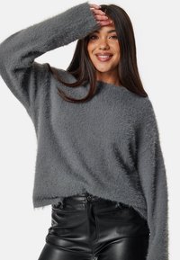 Maglione grigio morbido con una vestibilità over e maniche ampie; presenta un orlo grezzo e una texture soffice, abbinato a pantaloni in pelle nera.