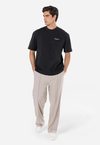 Tricou negru cu mânecă scurtă, cu logo brodat, asociat cu pantaloni bej deschis. Material moale, cu o croială confortabilă și un design minimalist.