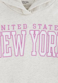 Felpa beige con "UNITED STATES" in piccole lettere rosa e "NEW YORK" in grandi lettere bianche contornate di rosa sul petto.