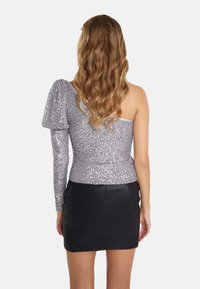 En skuldertop med glitrende sølvfarvede paljetter, der har en voluminøs ærme og en tætsiddende pasform. Kombineret med en sort miniskirt.