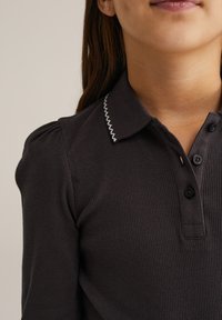 Polo gri închis cu nervuri și guler decupat, prezentând cusături în zigzag alb și trei nasturi negri în față. Pliuri subtile pe umeri.