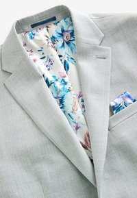 Veste de costume gris clair avec doublure intérieure à motif floral et pochette assortie à motif floral.