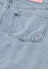 Světle modrá džínovina s zadním kapsou s malou výšivkou růžového srdce. Hladká textura s viditelnými švy.