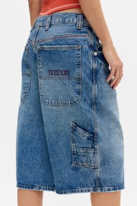 Bermudas de denim en azul claro con una textura deslavada. Presenta dos bolsillos traseros y un bolsillo lateral tipo cargo con costuras en contraste y un logotipo bordado.