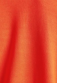 Gros plan d’un tissu texturé orange vif avec un motif tissé visible et des plis souples créant des variations de lumière et d’ombre.