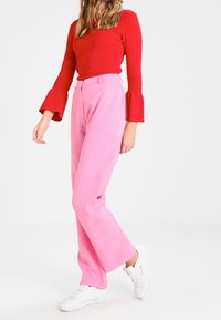 Rood langemouwtop met uitlopende manchetten, gecombineerd met hoogwaardig roze wijde broek en witte sneakers. Glad materiaal, felle kleuren.