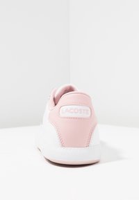 Baskets blanches avec un accent rose sur le talon, dotées d'un arrière texturé, d'un lacet à l'avant et d'un logo cousu. Matériau synthétique lisse.