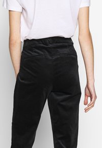 Svarta kordpants har hög midja, sidofickor och en slät yta, med en enkel design och utan synliga mönster eller detaljer.