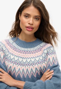 Strickpullover in sanftem Blau mit einem mehrfarbigen Muster aus Herzen und Zickzacklinien in Weiß, Pink und Marineblau. Gerippter Halsausschnitt und Bündchen.