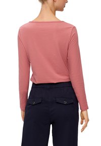 Langärmliges Oberteil aus weichem pinken Baumwollstoff, mit einem quadratischen Ausschnitt und lässiger Passform. Kombiniert mit Marineblauen Hosen mit geknöpften Gesäßtaschen.