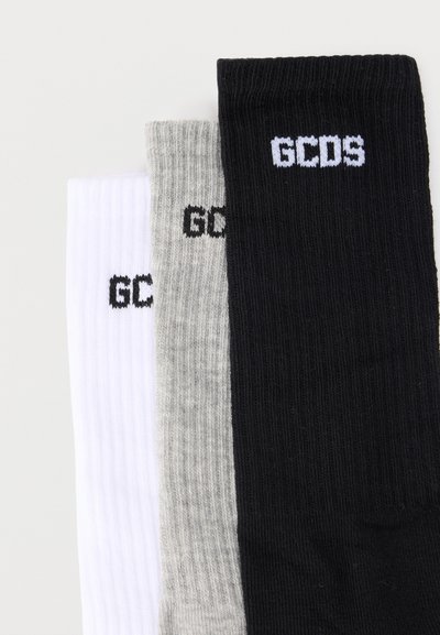 Trois chaussettes mi-mollet à côtes en blanc, gris et noir, chacune avec le logo "GCDS" brodé près du bord-côte.