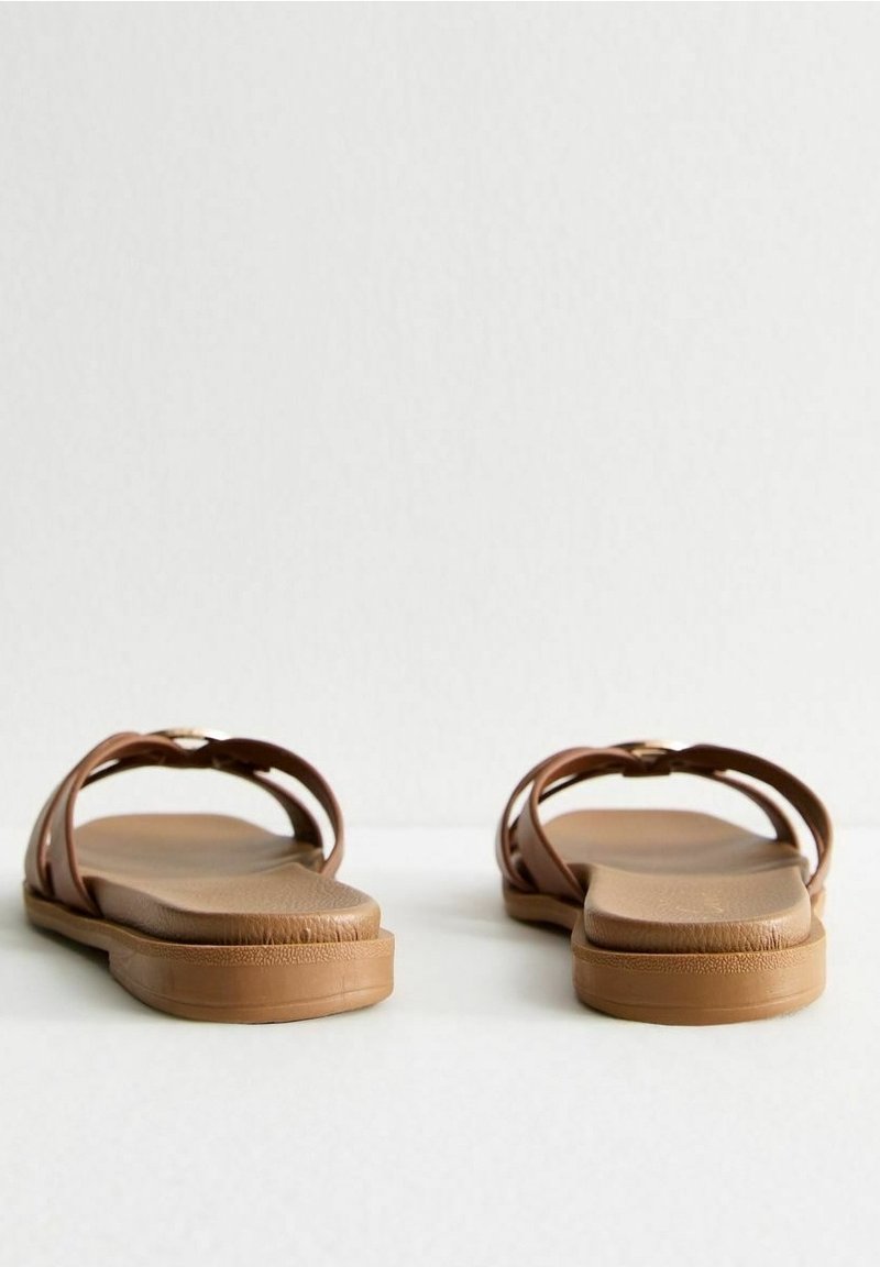 Paire de sandales plates marron avec des larges brides, vues de face sur un fond clair uni.