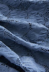 Modrý krajkový materiál s texturovaným květinovým vzorem, který má složité otevřené tkaní a jemné, delikátní splývání.