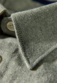 Hemd mit Kragen aus grauem, strukturiertem Stoff mit diagonalem Streifenmuster, Knopfdetails und spitzem Kragen.