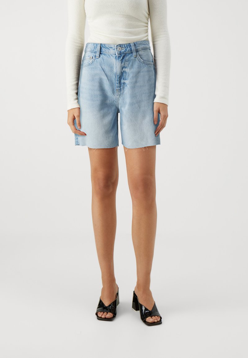 Lys blå denimshorts med avslappet passform, med knappestolpe, frontlommer og frynset kant. Kombinert med svarte høyhælte sandaler.