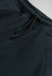 Close-up van een zwarte elastische tailleband met een gestrikt trekkoord aan een zachte stoffen broek.