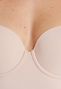 Sostenitore rosa chiaro imbottito con tessuto liscio, coppe arrotondate e una cucitura centrale. Presenta un bordo pulito e dettagli di cucitura lungo il colletto.