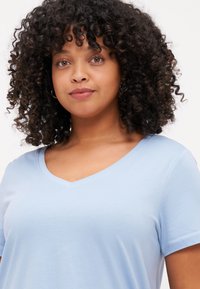 Camiseta de cuello en V azul claro, fabricada con tela suave, con mangas cortas y un ajuste relajado. Diseño minimalista sin patrones ni acentos.