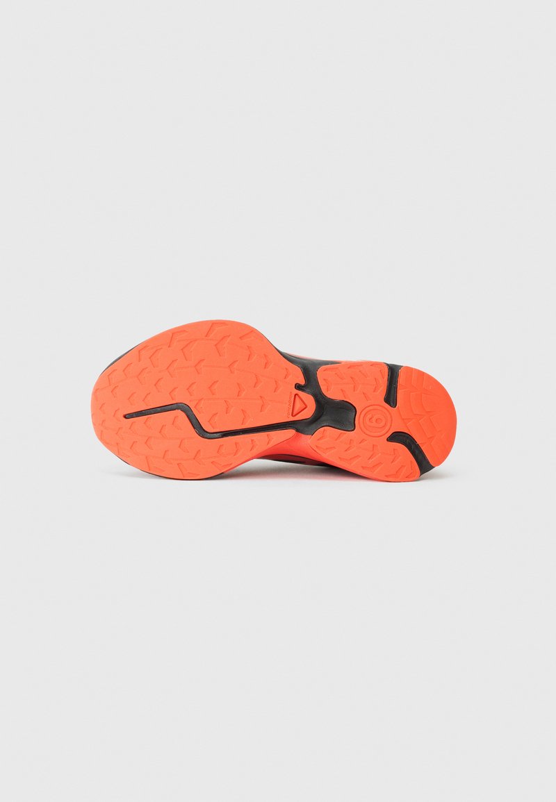 La semelle de chaussure présente une base noire avec du caoutchouc orange vif. Grip texturé avec des motifs en zigzag et une rainure centrale pour l'adhérence.