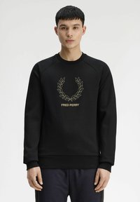 Felpa nera con collo rotondo, polsini e vita a costine. Presenta una ghirlanda di alloro ricamata in oro e il logo "FRED PERRY" al centro.