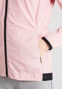 Hellrosa wasserdichte Jacke mit schwarzem Reißverschluss, Seitentaschen und elastischen Bündchen. Verfügt über eine dezente Textur und ein Logodetail am Saum.