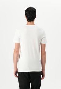 T-shirt branco de manga curta com decote redondo, textura suave e design minimalista, visto por trás.