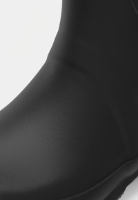 Czarny gumowy but o gładkiej, teksturowanej powierzchni i lekkim wyprofilowaniu w okolicy kostki, z wzmocnioną podeszwą dla zwiększonej trwałości.