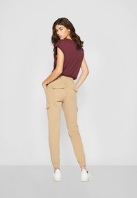 Burgunderfarget t-skjorte med korte ermer, kombinert med beige cargo-bukser med elastiske mansjetter og baklommer, akkompagnert av hvite sneakers.
